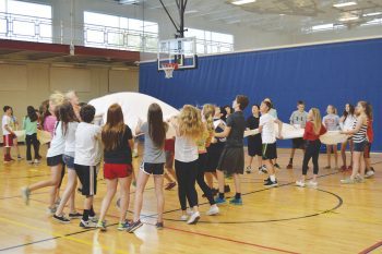 A group of students in an indoor gym play with a parachute