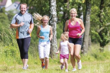 Family jogging through a field on the edge of a low density forest