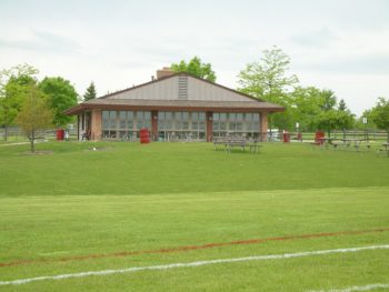 Ron Beese Park shelter, viewed from the adjacent soccer field. There is a closed shelter, outdoor seating, and plenty of trash cans.