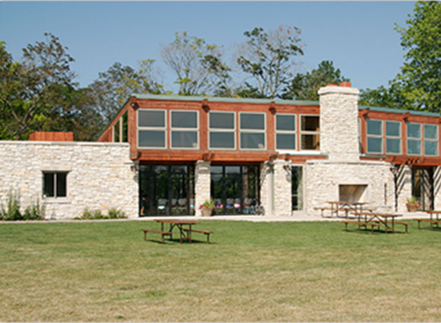 Jewel Tea Pavilion. View of a field with some benches in front of a large, 2-story stone and cedar building