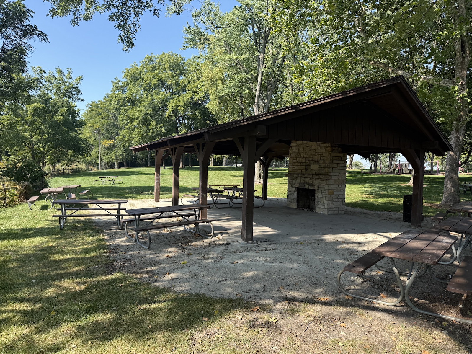 Picnic shelter with wooden pavilion, picnic tables, and grill in a shaded park.