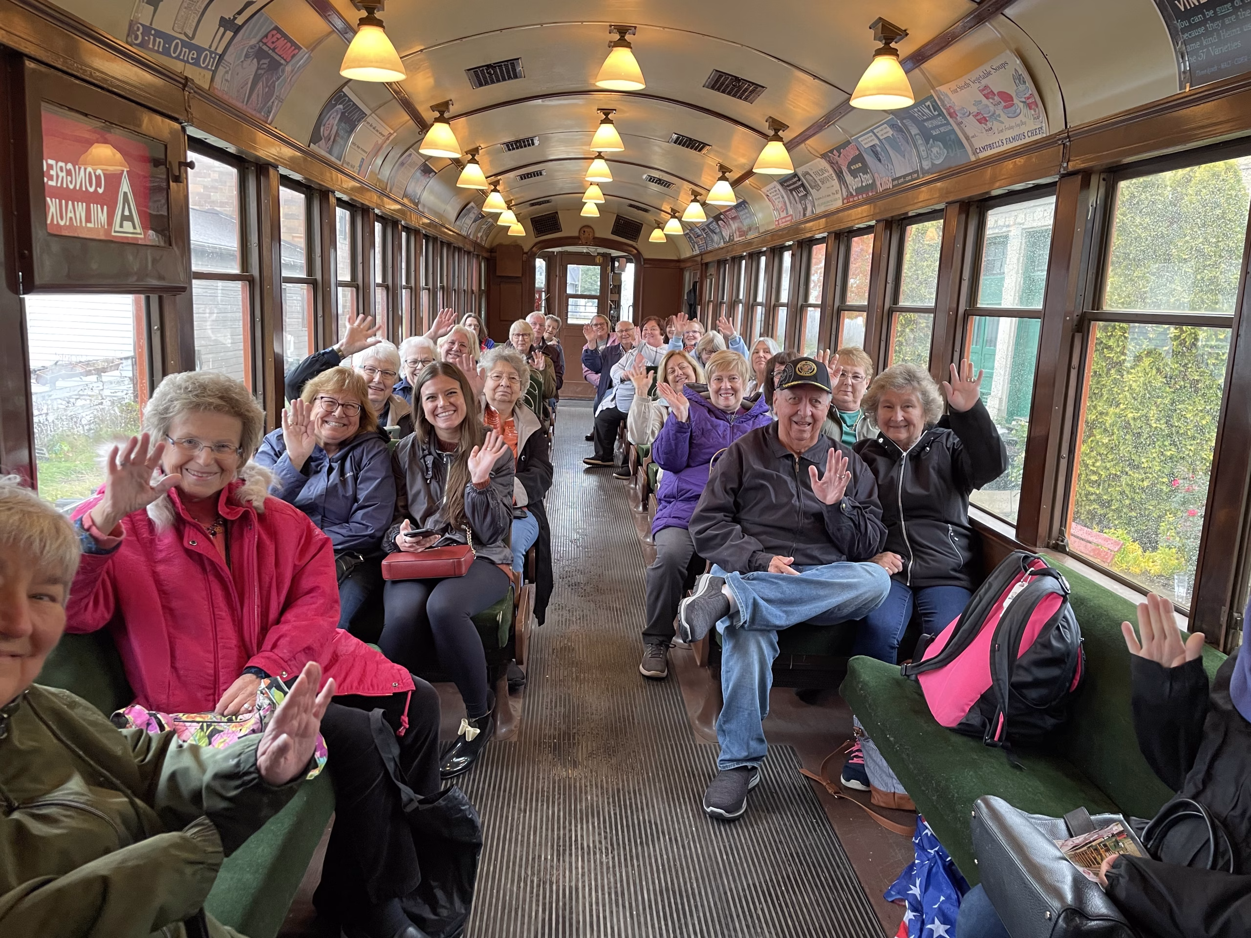 A large number of seniors sitting in a train car smile and wave for the camera.